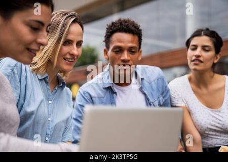 Diverse group of freelance contractor looking at a laptop's screen in an outdoors setting Stock Photo