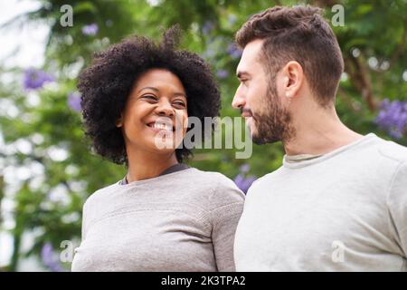 Mid-shot portrait of an African-American woman and Caucasian man smiling at each other and having a good time outdoors Stock Photo