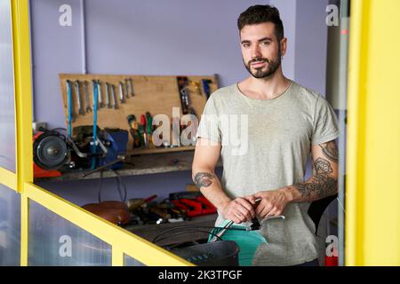 Mid-shot portrait of bearded man standing in his workshop in front of his tools Stock Photo