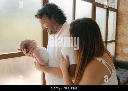 From above Hispanic parents embracing and admiring infant while sitting near pillows in bedroom at home Stock Photo