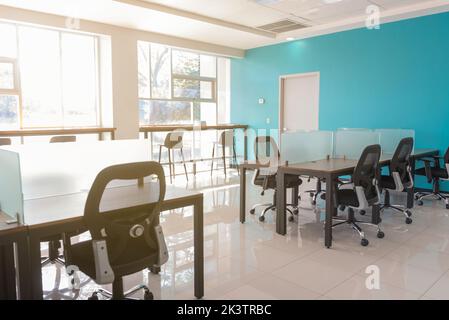 Interior of modern coworking space with office chairs placed at wooden table with glass dividers in sunlight Stock Photo