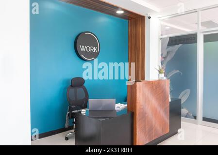 Comfortable chair at reception desk with laptop and documents in modern office space with blue wall Stock Photo
