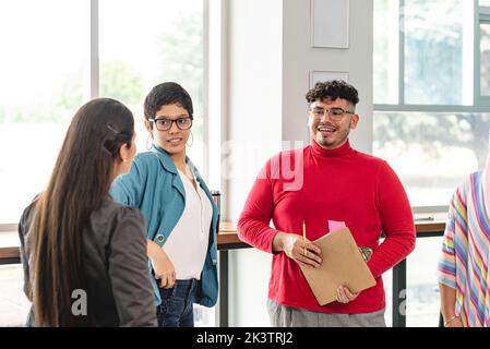 Positive Hispanic coworkers in casual clothes standing and talking with unrecognizable woman manager in light office in Costa Rica in daytime Stock Photo