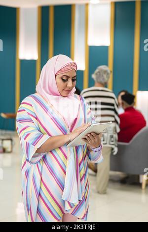 Muslim woman in pink hijab and colorful dress standing with tablet while working in modern workspace in Costa Rica in daytime Stock Photo
