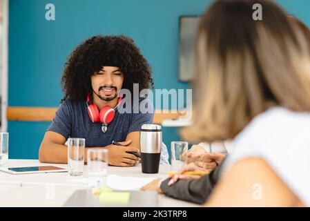 Group of multiethnic coworkers sitting at table and talking to each other about new business strategy during meeting in workspace in Costa Rica Stock Photo