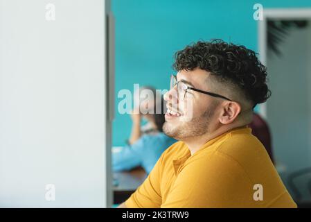 Side view of delighted Hispanic male worker with Afro hairstyle laughing in creative workspace and looking away in Costa Rica Stock Photo