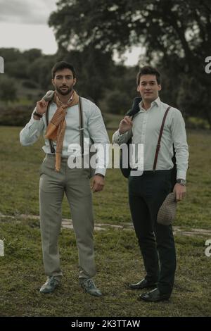 Handsome guys in shirts and trousers with suspenders looking at camera on a cloudy day at meadow Stock Photo