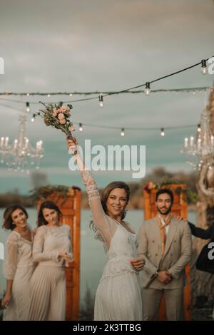 Bride with bunch of flowers in upped hand , guests celebrating at background Stock Photo