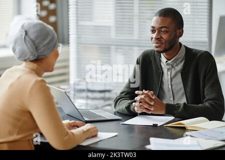 Portrait of young black man talking to HR manager in job interview and smiling Stock Photo