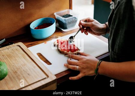 Crop unrecognizable cook preparing sandwich with tomato paste on white board Stock Photo