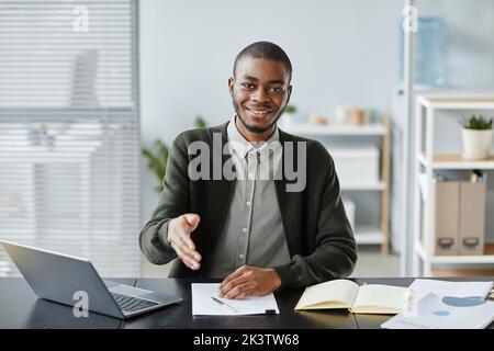 Front view portrait of young black man smiling at camera in job interview and holding hand for greeting Stock Photo