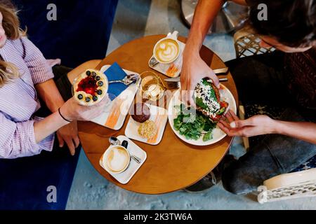 Crop unrecognizable people having breakfast sitting at a table in a cafe Stock Photo
