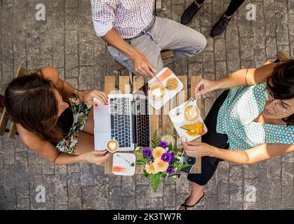 Crop unrecognizable people having breakfast sitting at a table in a cafe using laptop Stock Photo