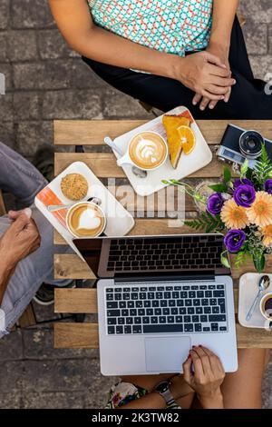 Crop unrecognizable people having breakfast sitting at a table in a cafe using laptop Stock Photo