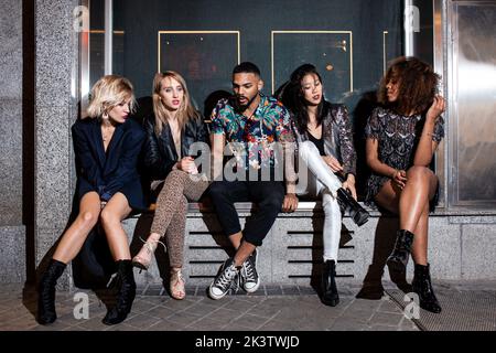 Trendy multiracial young friends together while sitting on concrete steps at night party Stock Photo