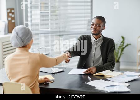 Portrait of young black man shaking hands with female HR manager after successful job interview in office, copy space Stock Photo