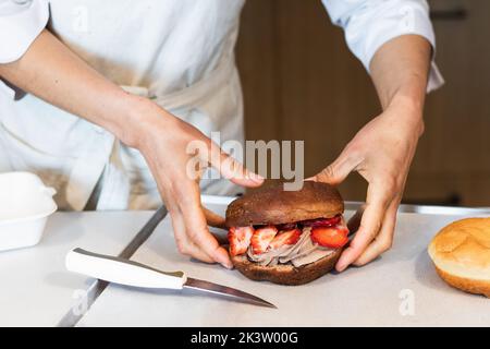 Crop unrecognizable baker holding sweet vegan sponge cake with whipped cream and strawberries in bakery Stock Photo