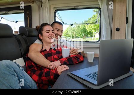 Content boyfriend embracing girlfriend while chilling in caravan and watching movie on netbook during trip Stock Photo