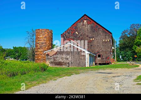 Old red barn in badly need of repairs, on a grassy field on a clear and sunny day -02 Stock Photo