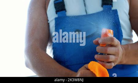 close-up, view through window, male cleaning service worker, in blue overalls, Cleaning Window by spraying Cleaning Products, using detergent, and rag. High quality photo Stock Photo