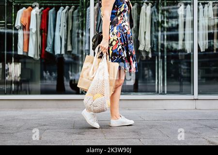 Sustainable Eco Friendly slow fashion Shopping. Faceless portrait of woman with white reusable canvas net bag and paper shopping bag on clothes shop Stock Photo