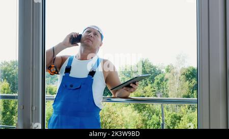 attractive Construction worker is discussing something on the phone, makes measurements of windows, makes notes in tablet. service man , builder examines the object. High quality photo Stock Photo