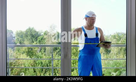 attractive Construction worker makes measurements of windows using measuring tape and make notes in tablet. service man installing window. High quality photo Stock Photo