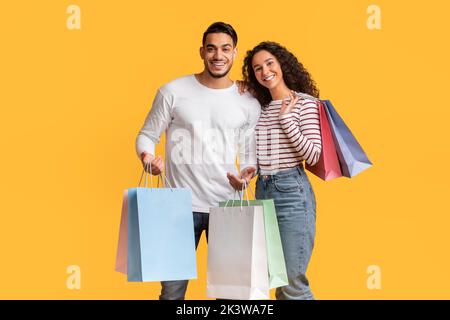 Middle Eastern Couple Posing With Shopping Bags In Hands Over Yellow Background Stock Photo