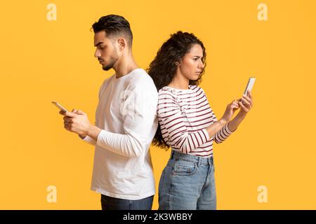 Gadget Addiction. Young Arab Couple Standing Back To Back And Using Smartphones Stock Photo