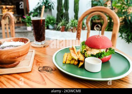 Vegan burger, in a red bun, dish with chips, on a green plate, on a wooden table, healthy vegetarian food. Stock Photo