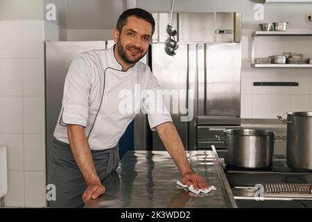 Young handsome male chef cleaning his workplace on kitchen in ...