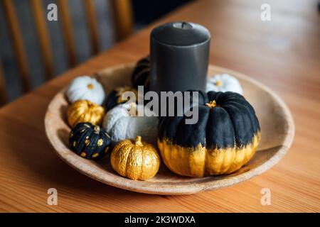 Black pumpkin halloween thanksgiving decor. Decorative modern minimal indoor composition with black, golden pumpkins in wooden plate at table Stock Photo