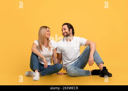 Happy handsome young caucasian couple look at each other, sit on floor Stock Photo