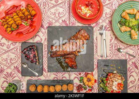 Several plates of food with croquettes, cones with salad, salmorejo, barbecue ribs, lemon cake and Russian salad with tomato and canned tuna Stock Photo