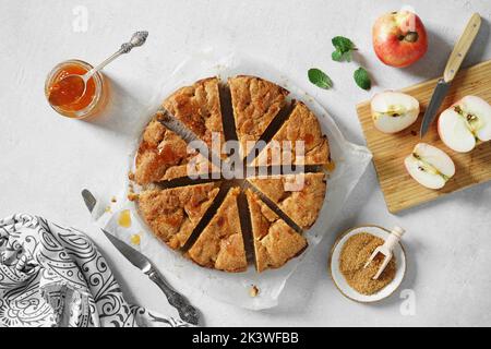 Freshly baked delicious apple pie with apricot jam cutting into pieces served on white light table. Stock Photo