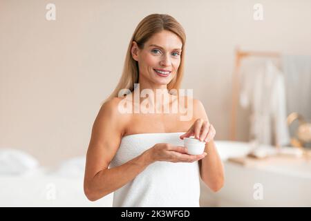 Skincare cosmetics. Happy middle aged woman trying new moisturising cream, making beauty routine at home Stock Photo