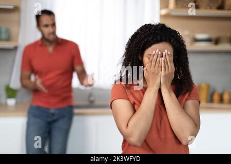 Sad angry millennial black male scolding to crying offended female in kitchen interior, free space Stock Photo