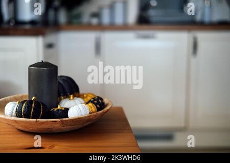 Black pumpkin halloween thanksgiving decor. Decorative modern minimal indoor composition with black, golden pumpkins in wooden plate at table Stock Photo