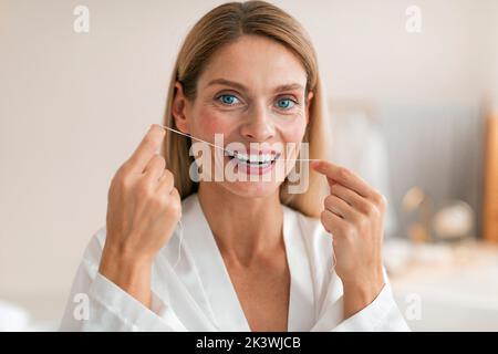 Oral health concept. Middle aged woman using dental floss, making daily hygiene, posing in bathroom interior Stock Photo