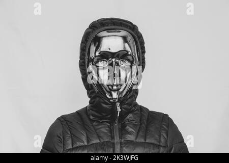 Girl in a faceless plastic mask and jackets with a hood on a white background black and white photo, anonymity, mystery Stock Photo