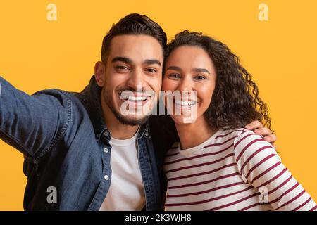 Romantic Cheerful Arab Couple Taking Selfie Together Over Yellow Background, Stock Photo