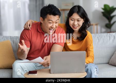 Happy asian spouses reading papers, using laptop at home Stock Photo