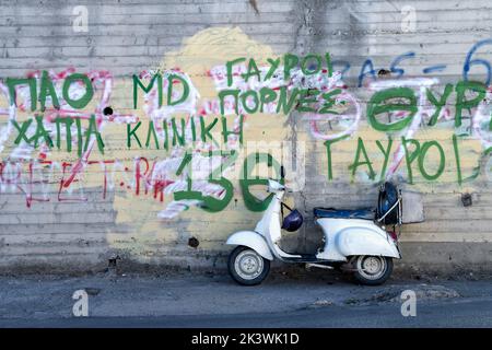A side view of an old classic Vespa scooter. The bike has been customised and hand painted in all over white paint. It’s parked by a graffiti wall Stock Photo