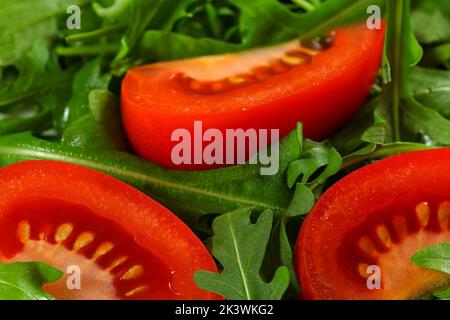 Closeup detail on bright red tomato slice and wet green arugula rocket leaves salad Stock Photo