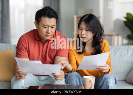 Upset asian couple checking bills, home interior Stock Photo