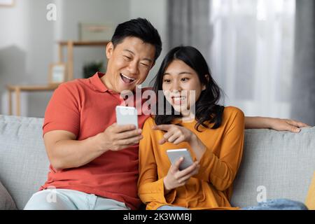 Cheerful chinese spouses using smartphones, home interior Stock Photo