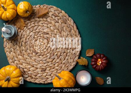 Cozy hygge table. Top view of wicker place mat, pumpkins, autumn leaves, candle on dark table. Autumn table setting. Festive Thanksgiving background. Stock Photo
