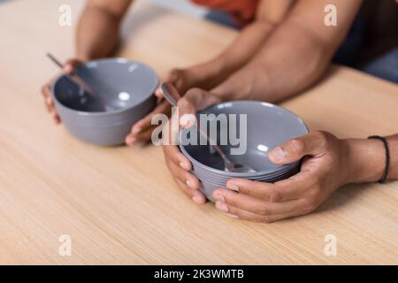 Sad millennial black wife and husband holding empty plates on wooden table, suffering from hunger Stock Photo