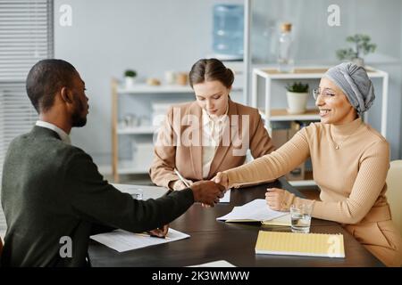 Diverse group of people in meeting or job interview at office setting, focus on Middle Eastern woman shaking hands with candidate Stock Photo