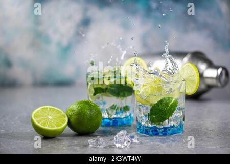 Summer alcoholic cocktail mojito with rum, mint, lime and ice, bar tools on concrete gray blue background. Mojito cocktail with splash and drops Stock Photo